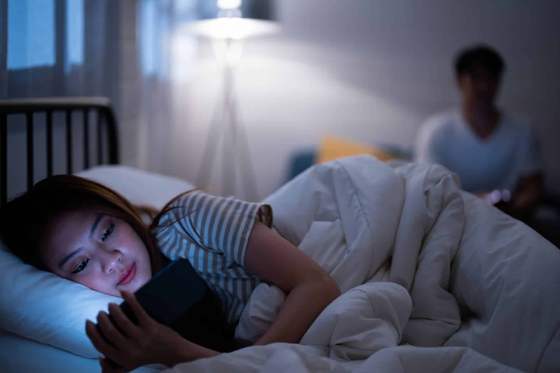 A woman is reading on her screen in bed before going to sleep, a bad habit she finds difficult to avoid, which is likely to disrupt her sleep.