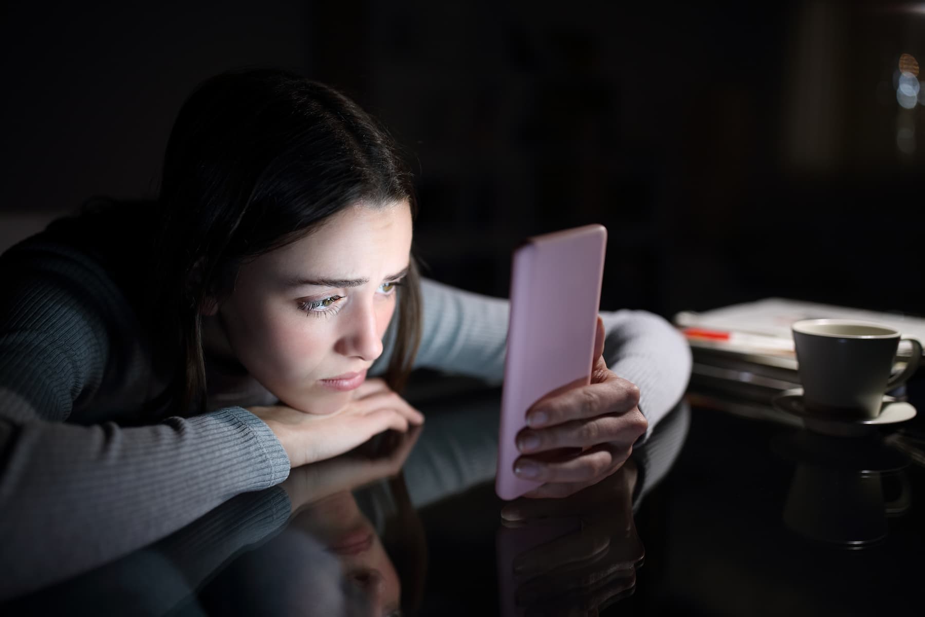 A sad woman is checking her phone at night, comparing herself to others on social media.