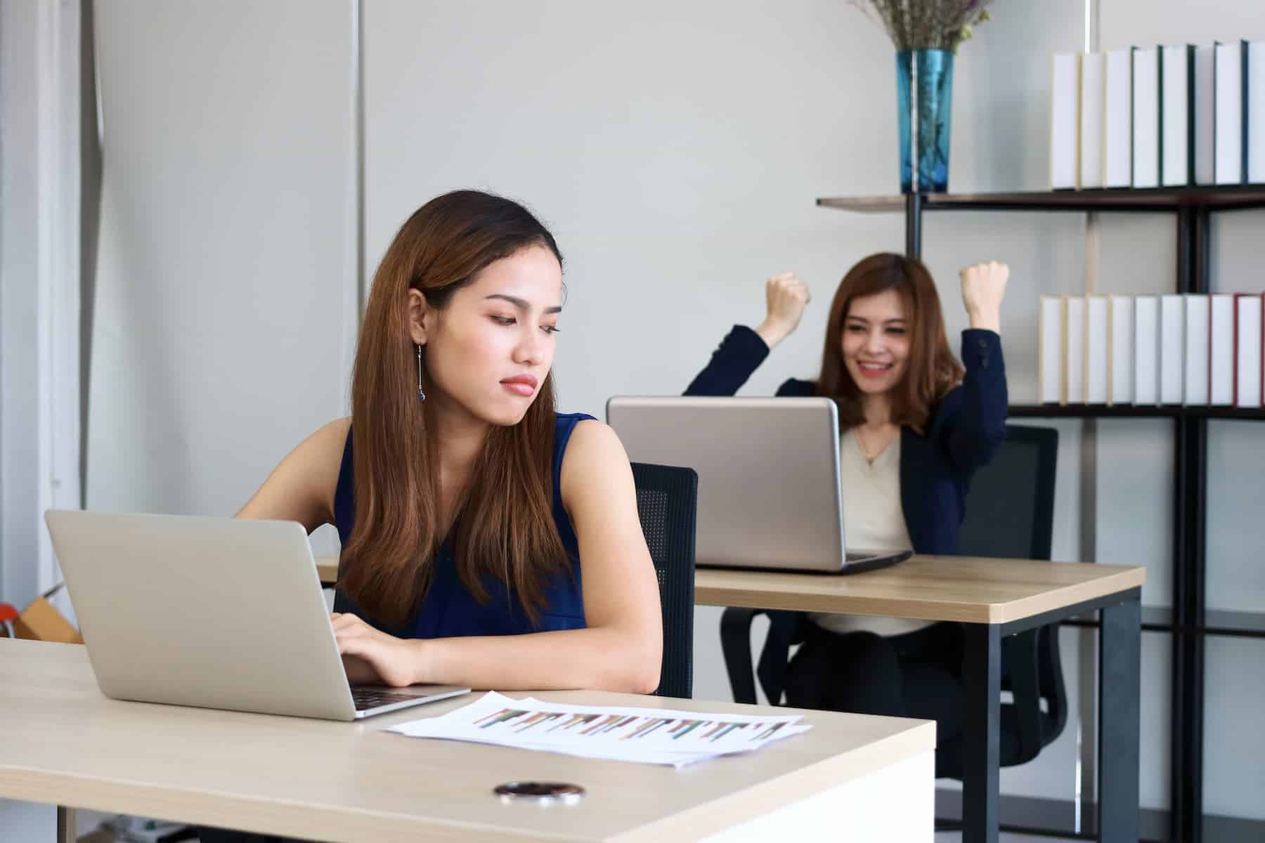 A young, angry, and envious businesswoman glares at her successful competitor colleague in the office.