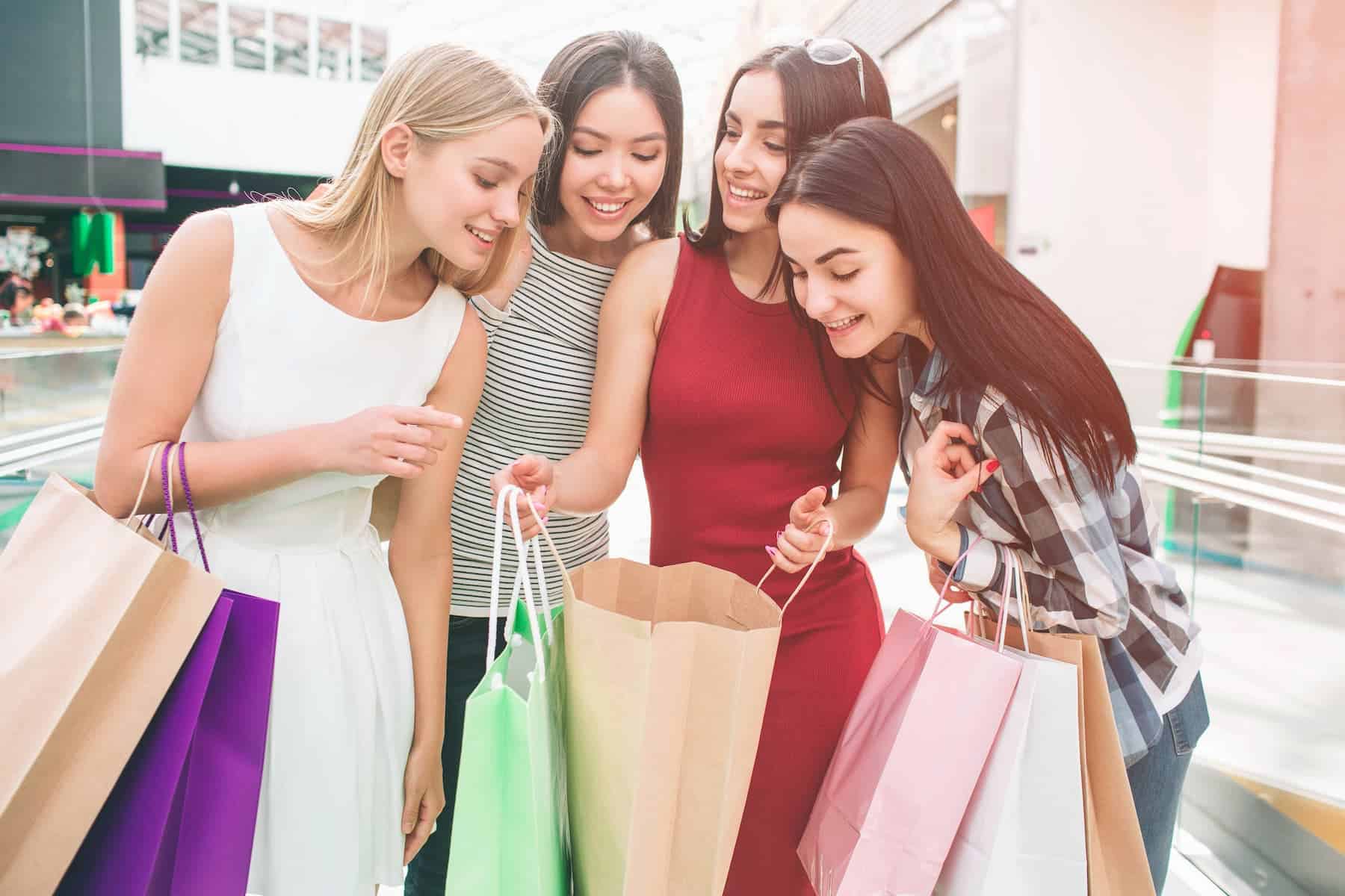 A group of young women stand together, peering into one girl's shopping bag, illustrating society's emphasis on consumerism and the reasons why we feel the need to hold onto material things.