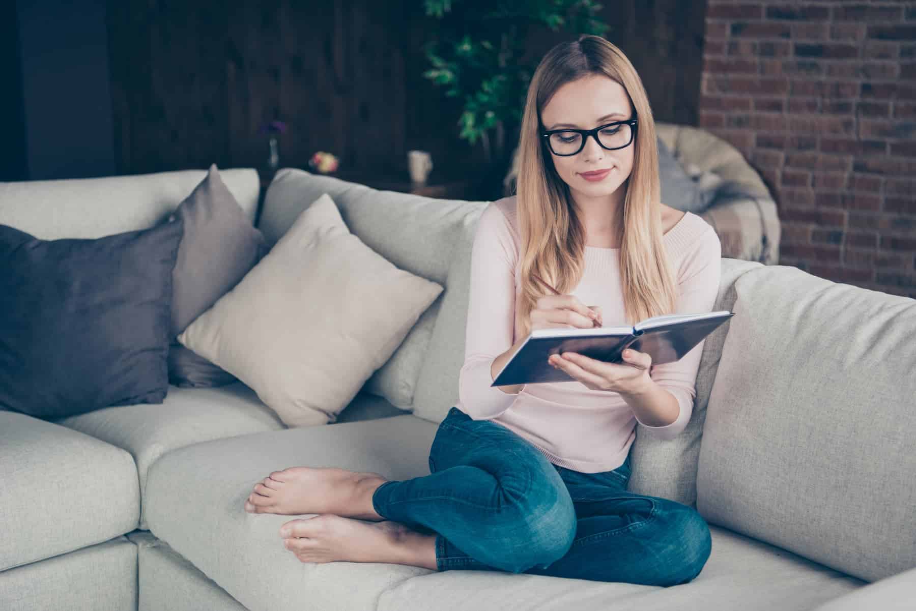 A young woman, as part of her effective daily routine, writes in her journal while seated comfortably on the couch.