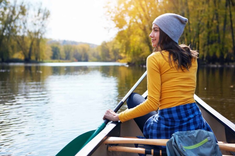 A highly sensitive woman is enjoying a quiet, solo canoe ride on the lake, finding peace and solitude as an introvert.