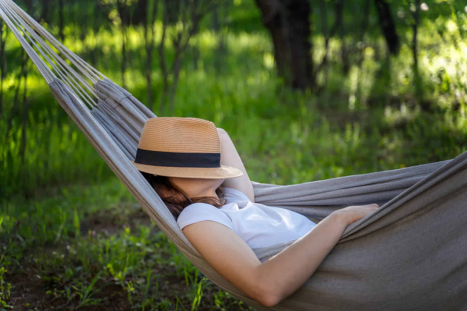 A young woman is taking a brief micro-break, with a hat covering her face, in a meadow as part of her daily routine to better manage stress.