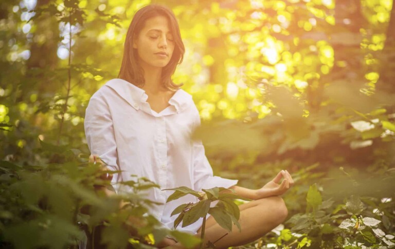 Woman finding balance within by doing meditation in nature to reduce stress and anxiety.