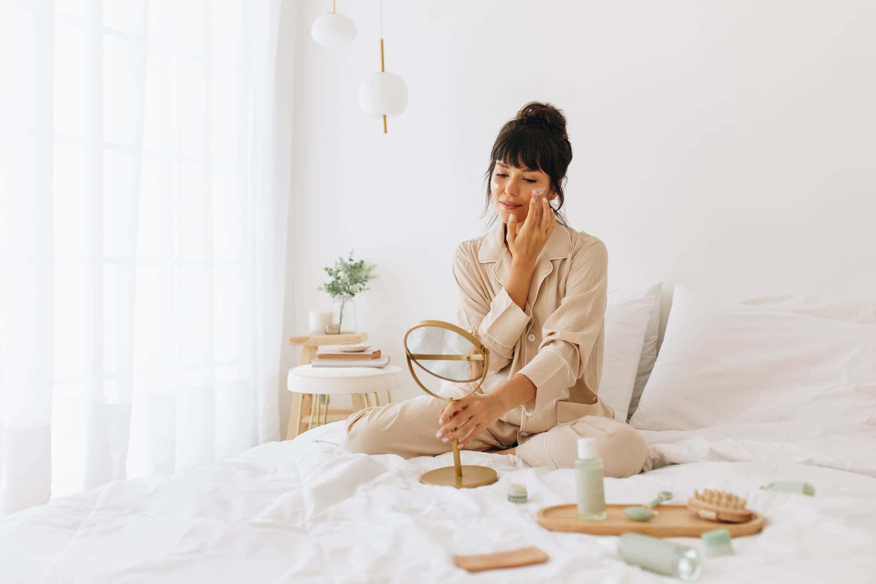 Self-care can take a negative turn when it becomes a form of avoidance, as seen with the young woman sitting on her bed surrounded by cosmetics, looking at herself in the mirror.