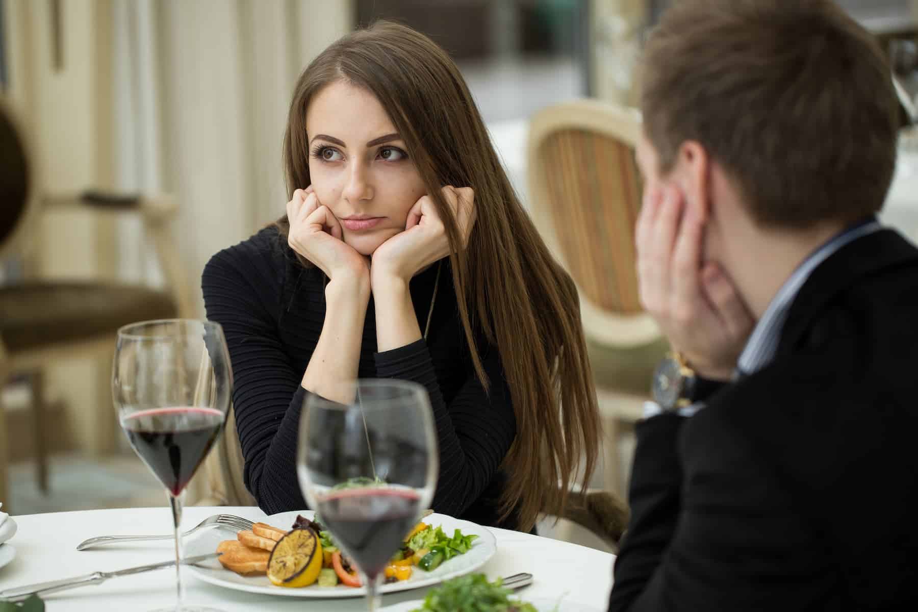 A young couple, bound together more by social status and vanity than genuine connection, sit through a dinner at a restaurant, their unhappiness evident despite the lavish surroundings.