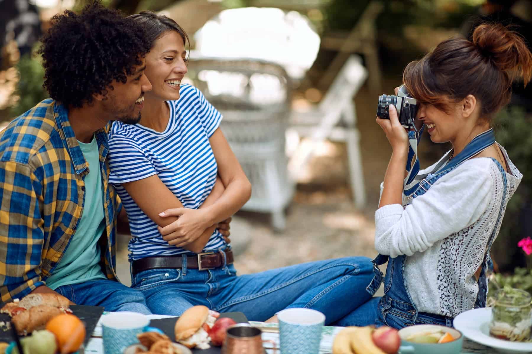 A young woman is capturing a moment with her friends in the backyard of a bar on a beautiful day. They cherish their bond of true friendship as they enjoy each other's company.