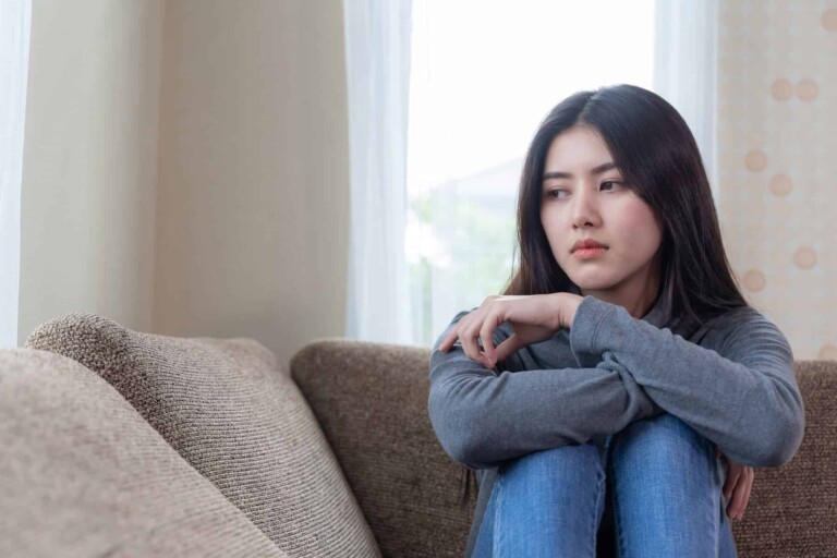 A young woman sits on sofa, overwhelmed by sadness as she comes to grips with why mediocrity is bad and the trade-offs she has had to make as a result.