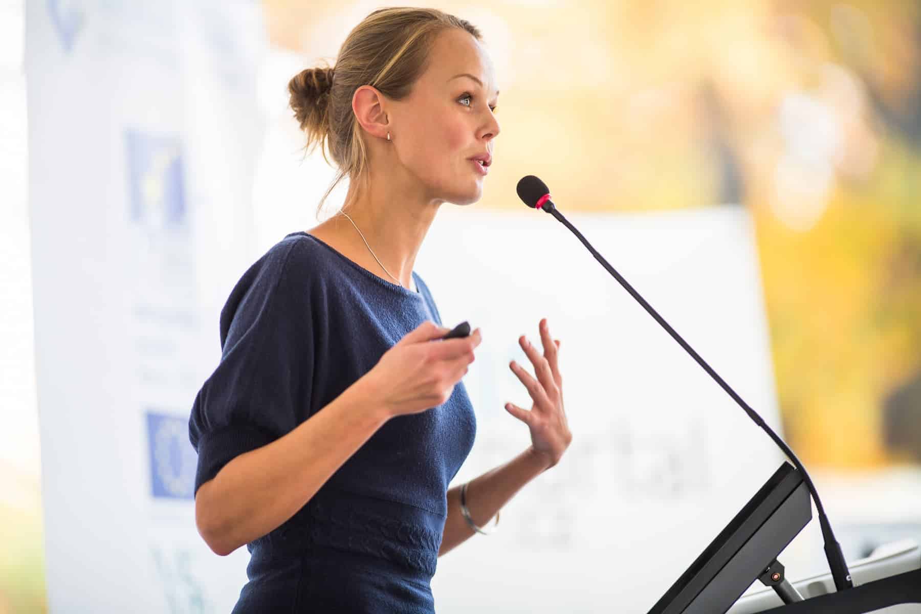 A businesswoman is giving a presentation at a conference, having applied the WOOP process to improve her public speaking skills.