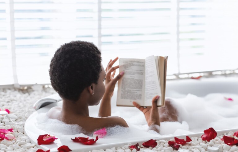 Young woman is relaxing in a hot tub with rose petals is reading a book as a self-care in her daily routine for her wellbeing.