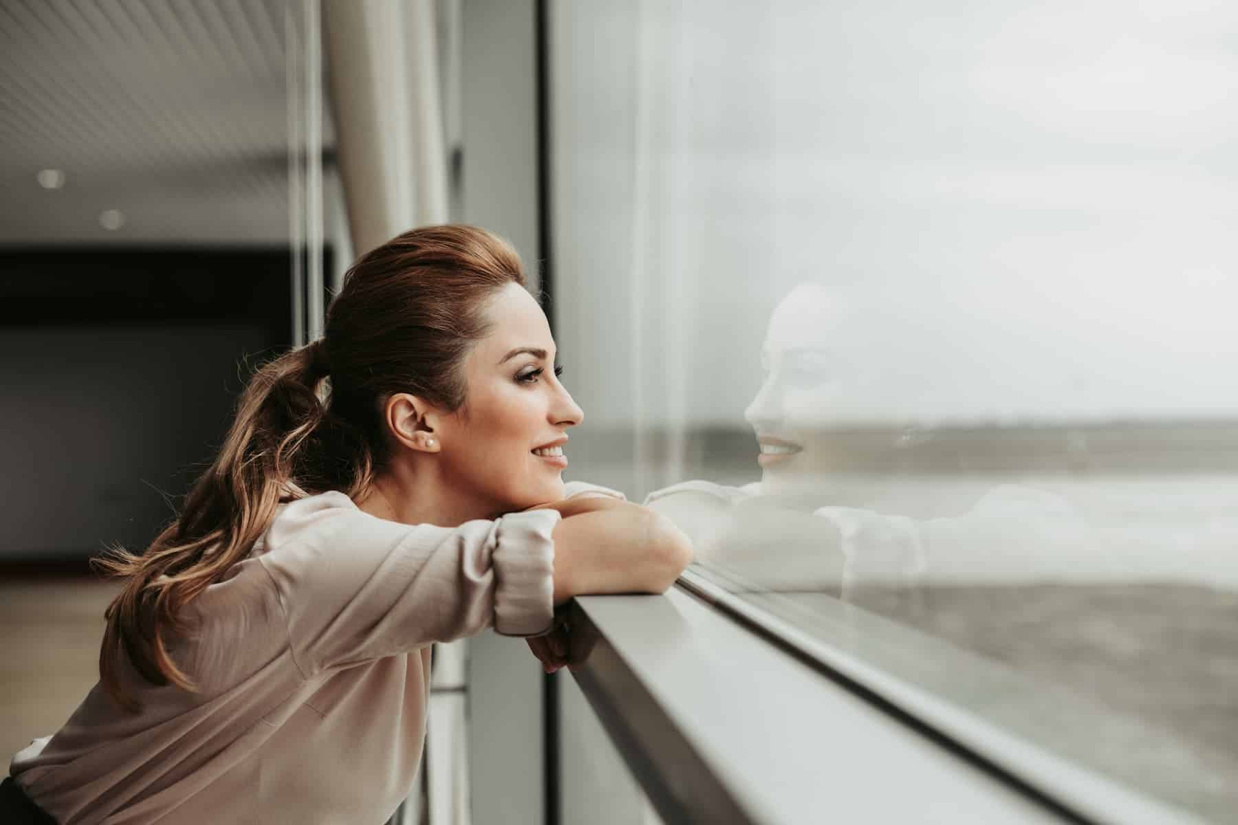 A young woman, smiling as she gazes out the window, is thinking about her wishes and hoping they will come true.