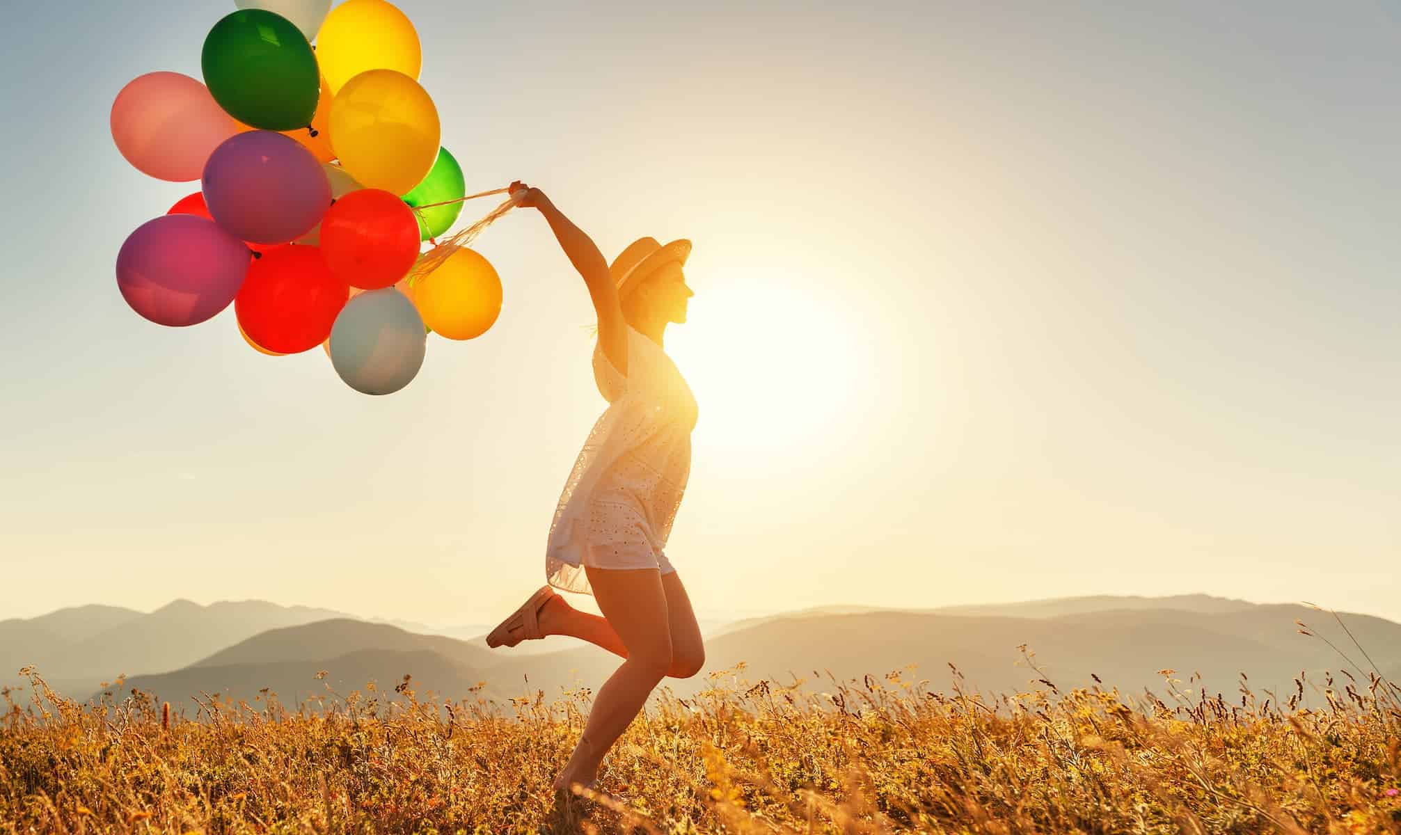 Young happy woman with balloons at sunset in summer. Being out in nature is one of the things a highly sensitive people need to be happy.