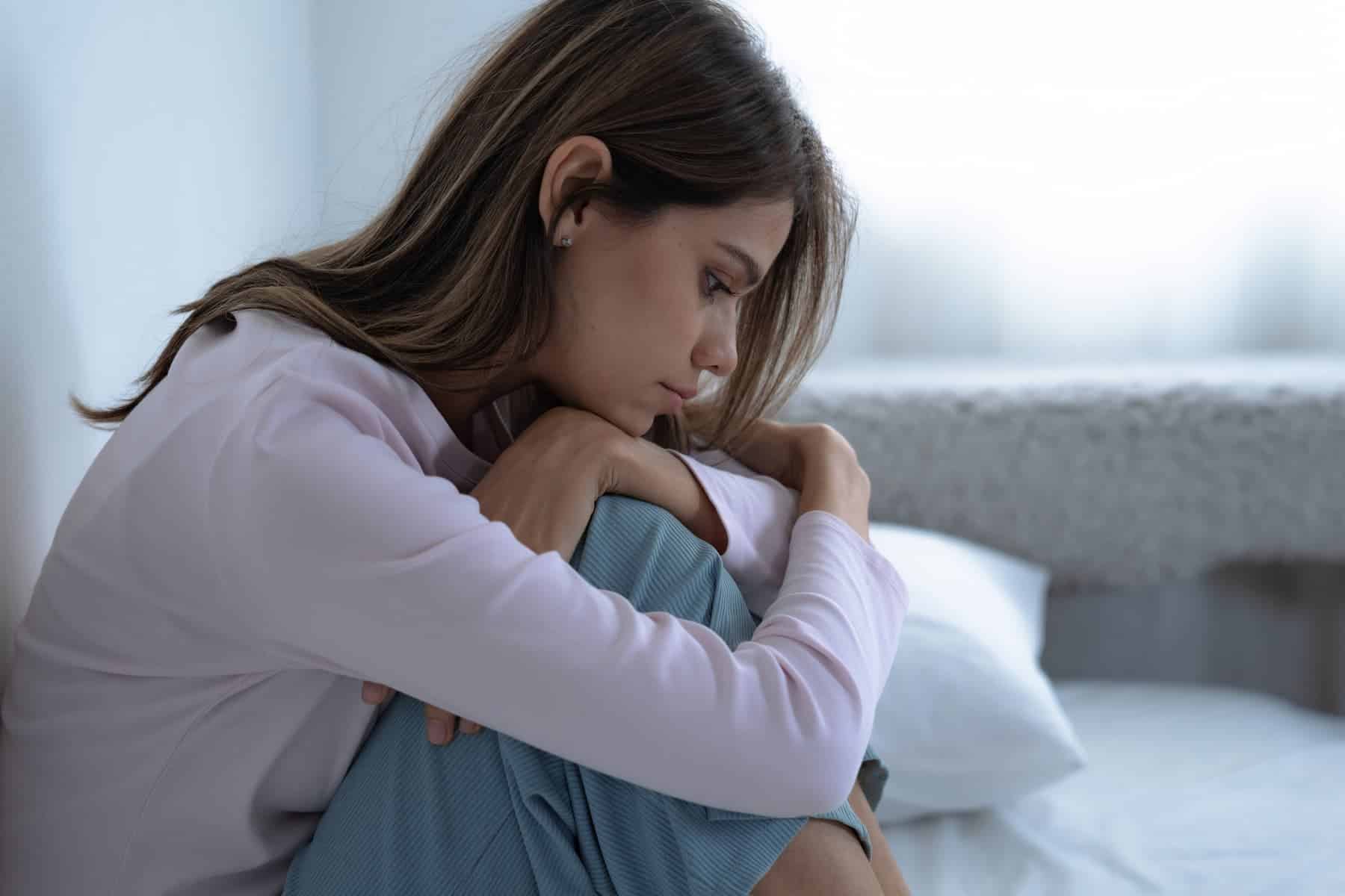 A young woman sitting on her bed, overthinking, displaying the signs of being a highly sensitive woman.