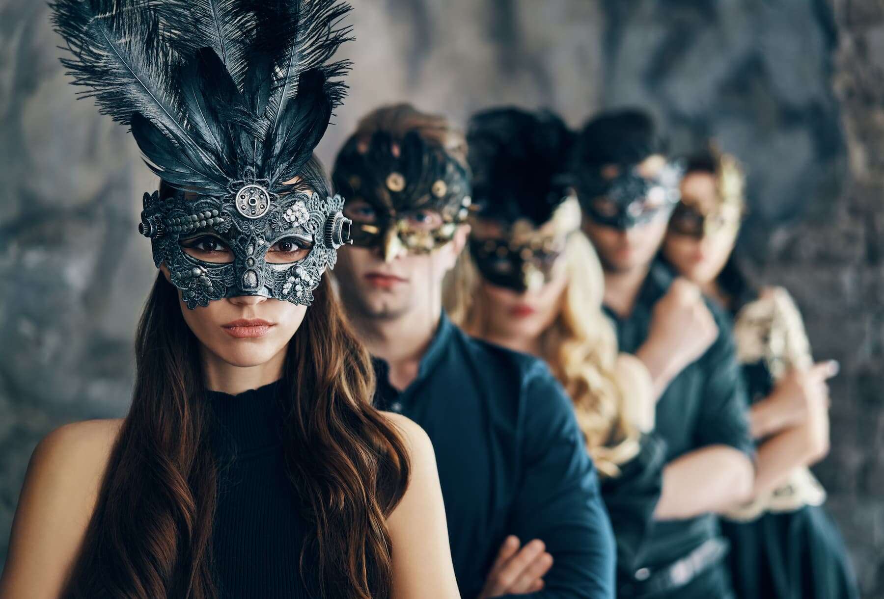 A group stands together in a studio, wearing masquerade carnival masks, each one symbolizing impostor syndrome and the feeling of being a fraud.