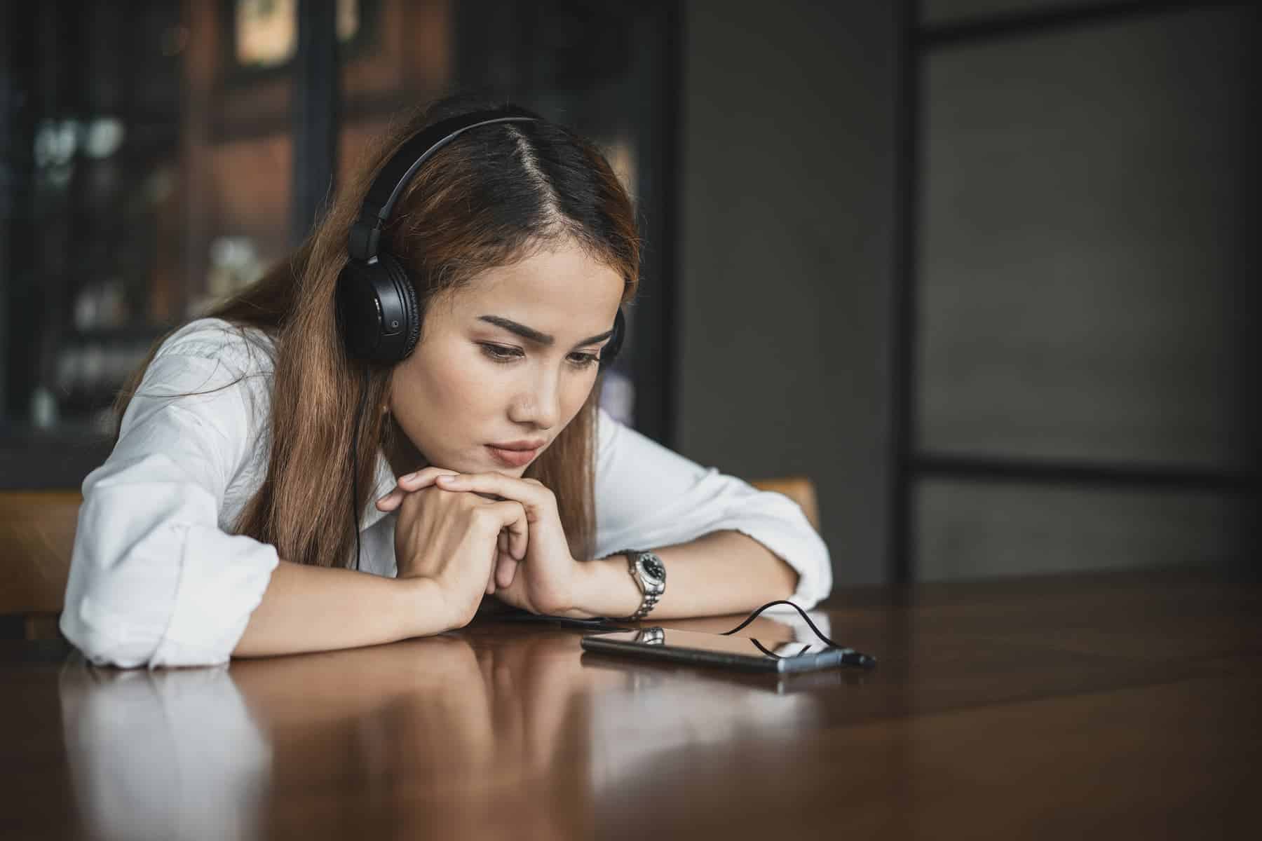A woman wearing headphones rests her chin on her hands while studying her phone.