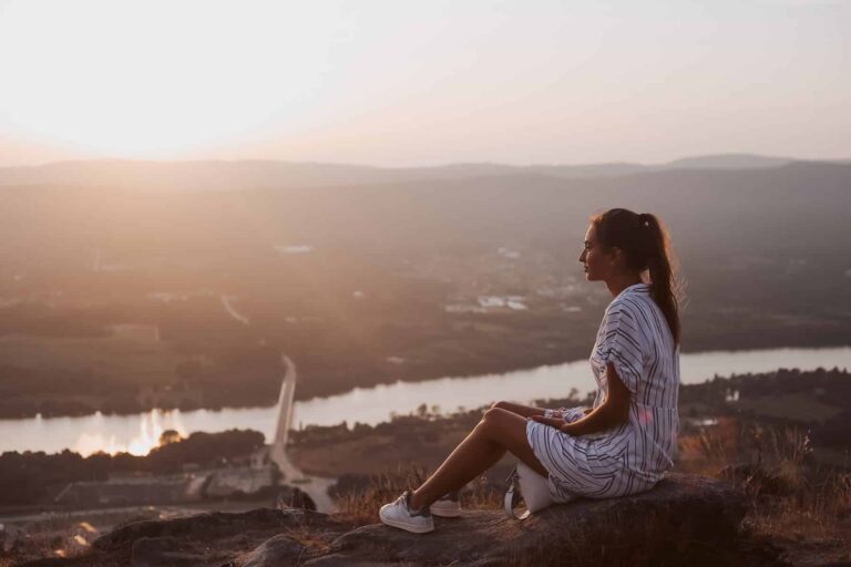 A woman relaxes on top of a hill overlooking the city, enjoying the view while practicing the law of detachment.