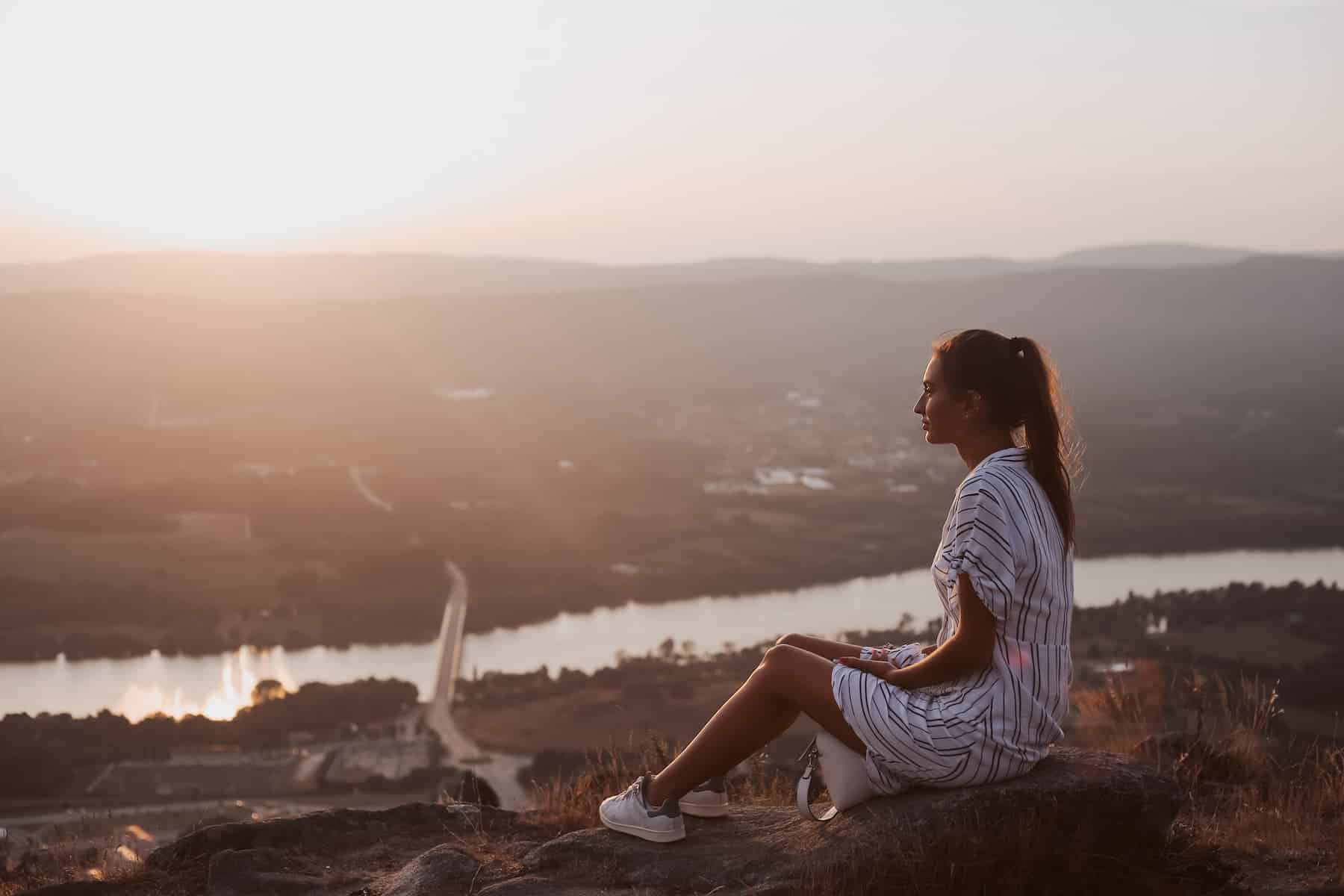 A woman relaxes on top of a hill overlooking the city, enjoying the view while practicing the law of detachment.