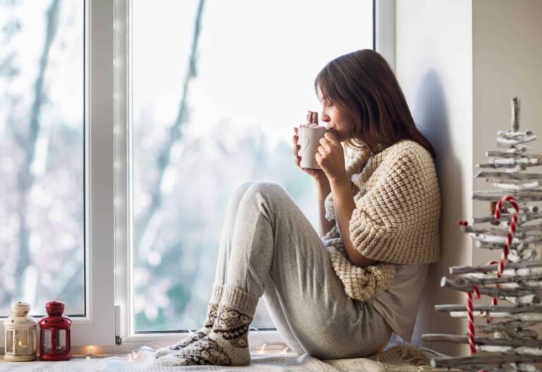 A woman finds solace in her comfort zone as she sits on the windowsill, sipping hot coffee, unaware of the need to break free.