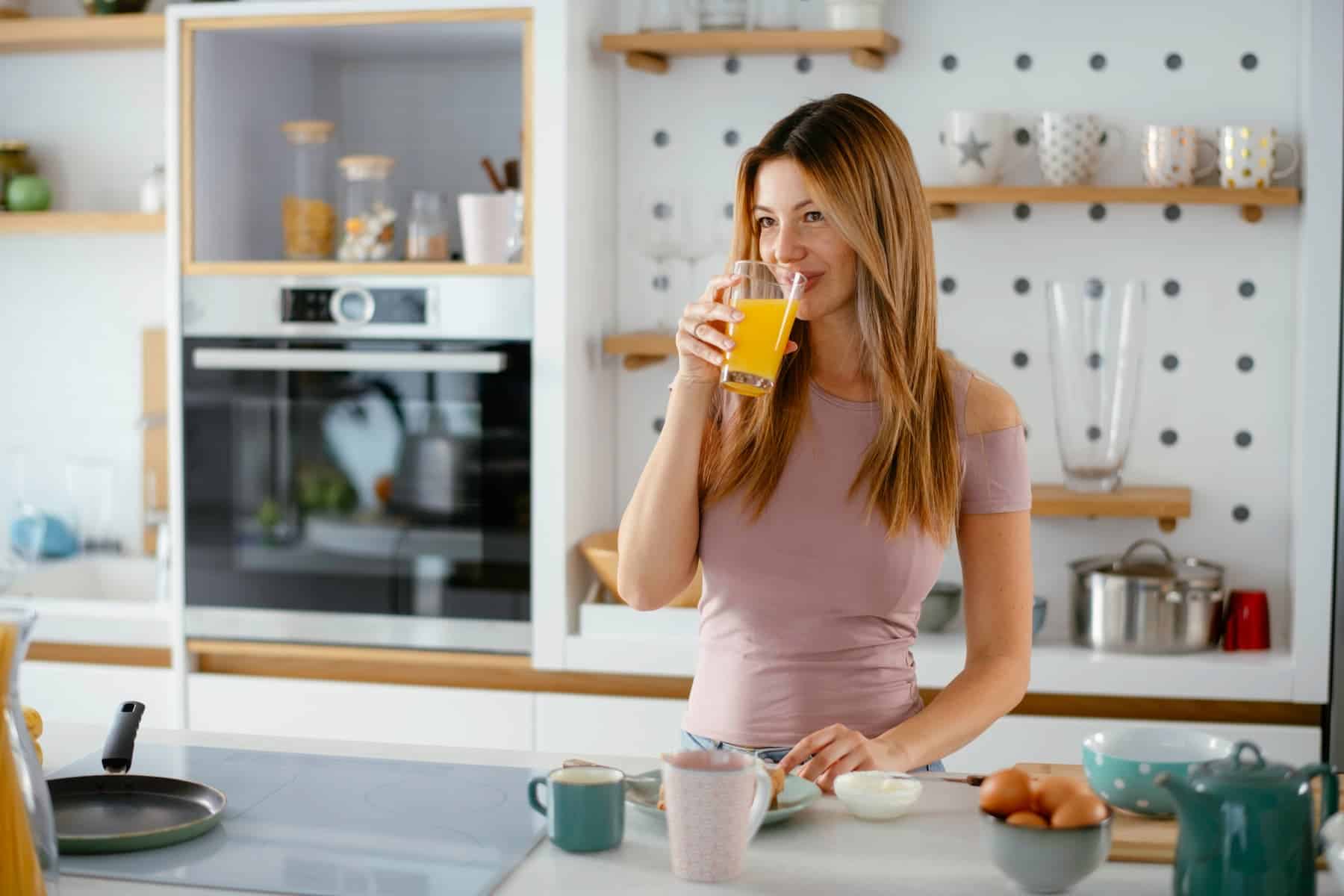 Young woman is enjoying fresh orange juice in the kitchen as part of her daily morning routine.