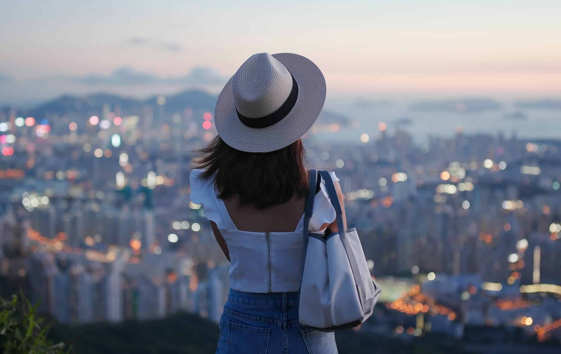 A woman wearing a hat enjoys a stunning city view at sunset from a hilltop, symbolizing the limitless energy of the quantum field.