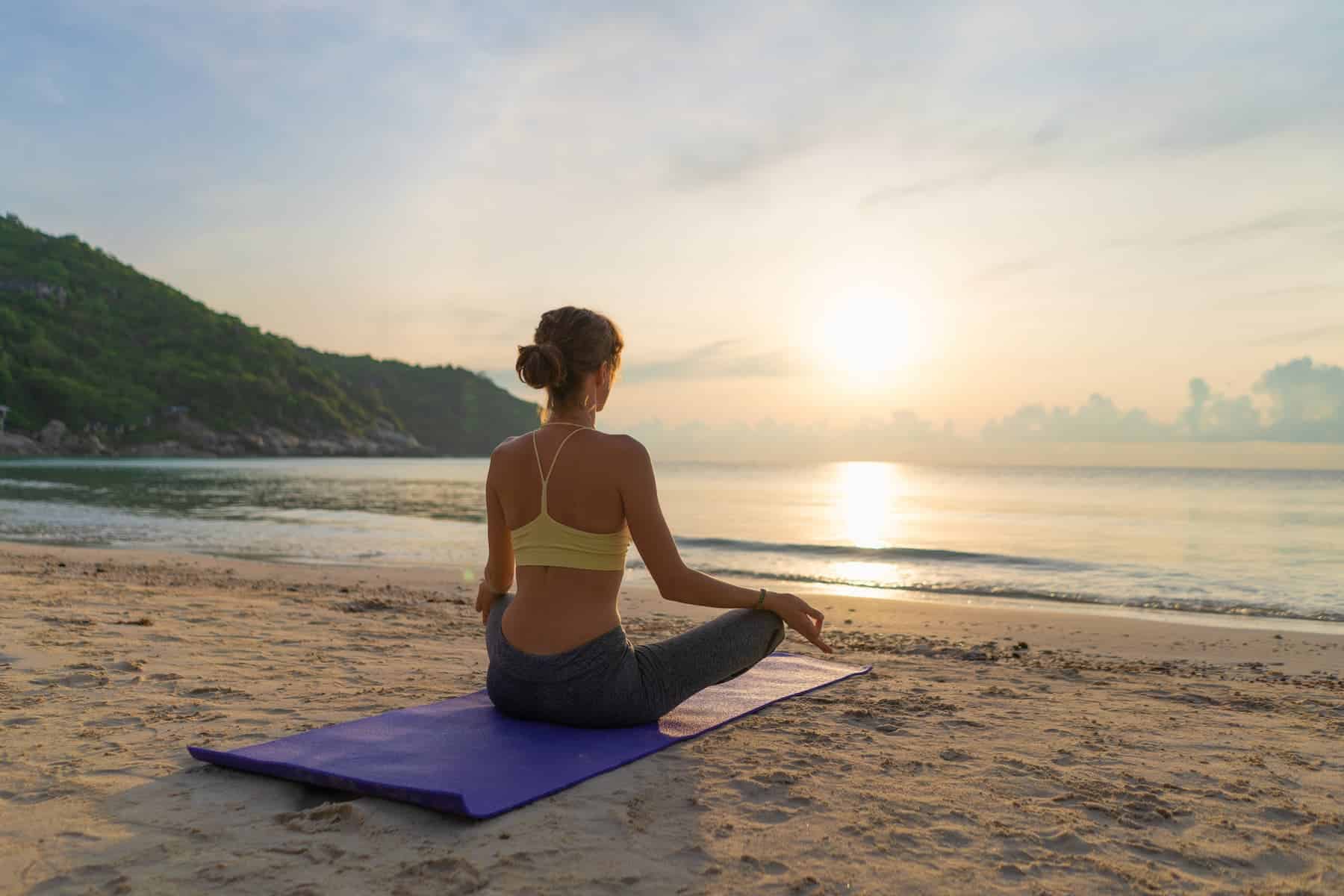 A calm woman sits in meditation by the ocean at sunrise, reflecting inner stillness connected to quantum physics spirituality.