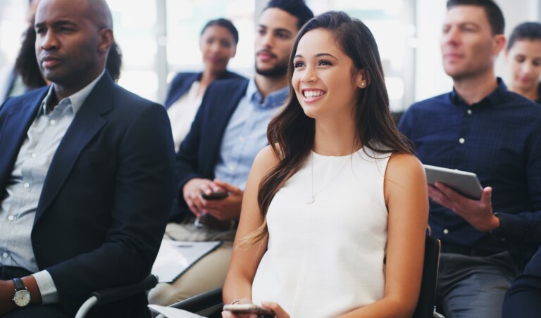 A woman in a white dress sits at a seminar, listening attentively and resolutely determined to succeed by not listening to the naysayers.