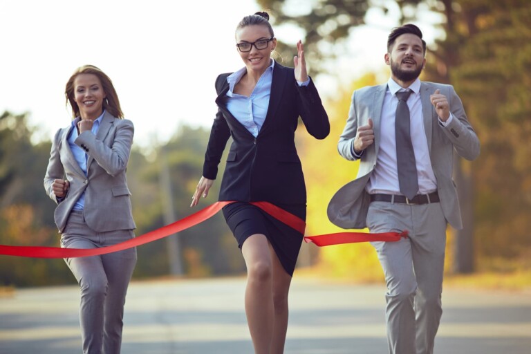 A businesswoman wearing glasses finishes first in a race against two colleagues, crossing the red ribbon. This scene exemplifies the journey from victim to victor.