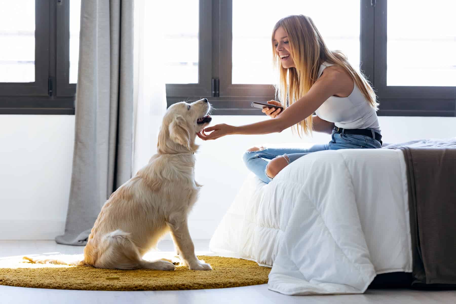 A young woman who is an empath sits on her bed using her phone, with her dog in front of her at home.