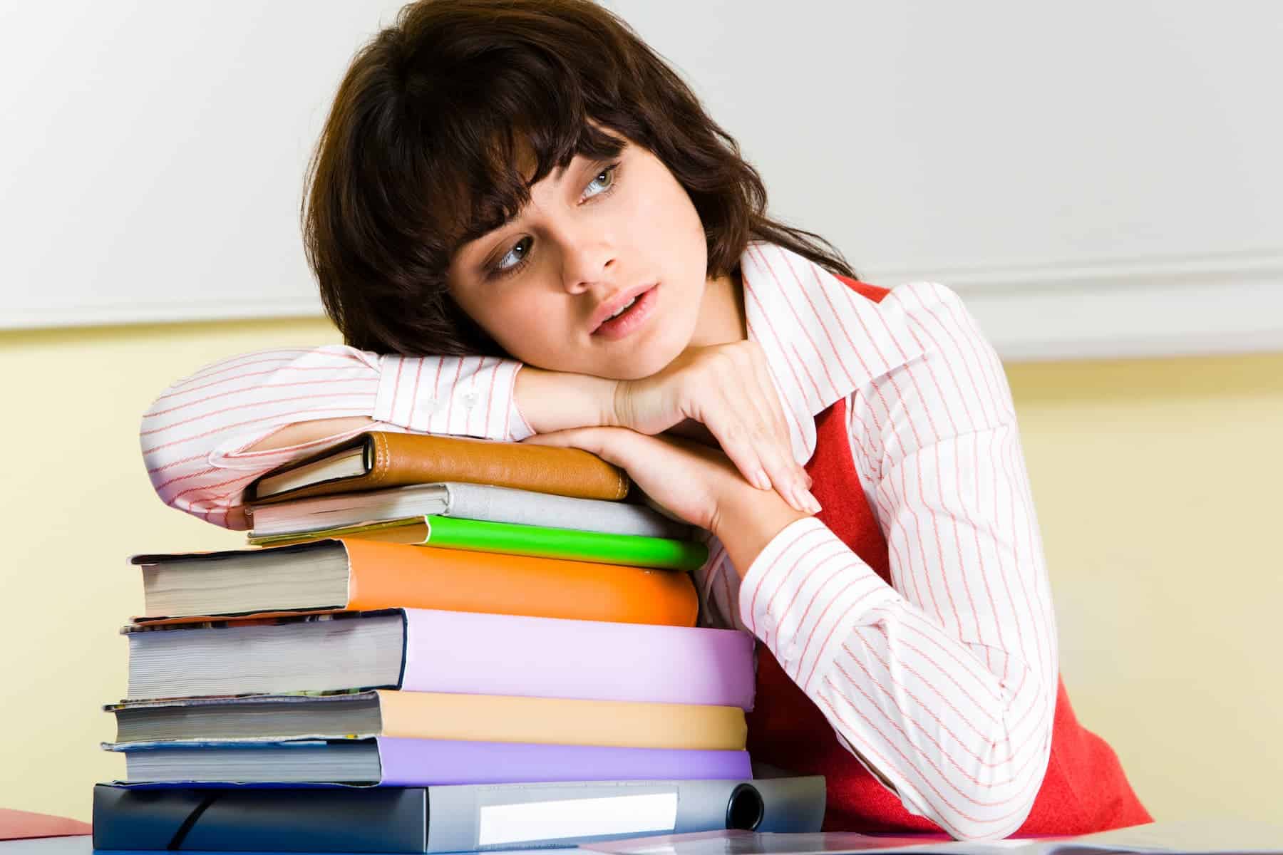 A woman appreciates the benefits of lifelong learning as she leans against a stack of books on her desk that she has already read.