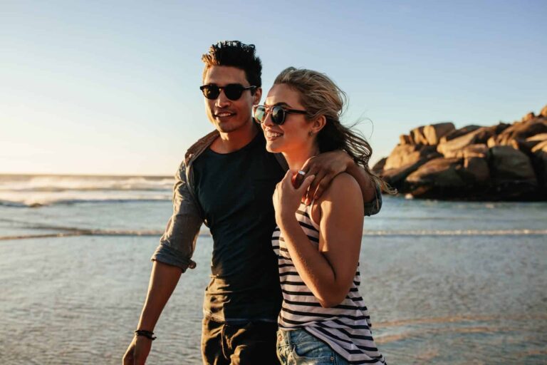 A happy empath woman walks along the beach with her boyfriend, enjoying their time together.