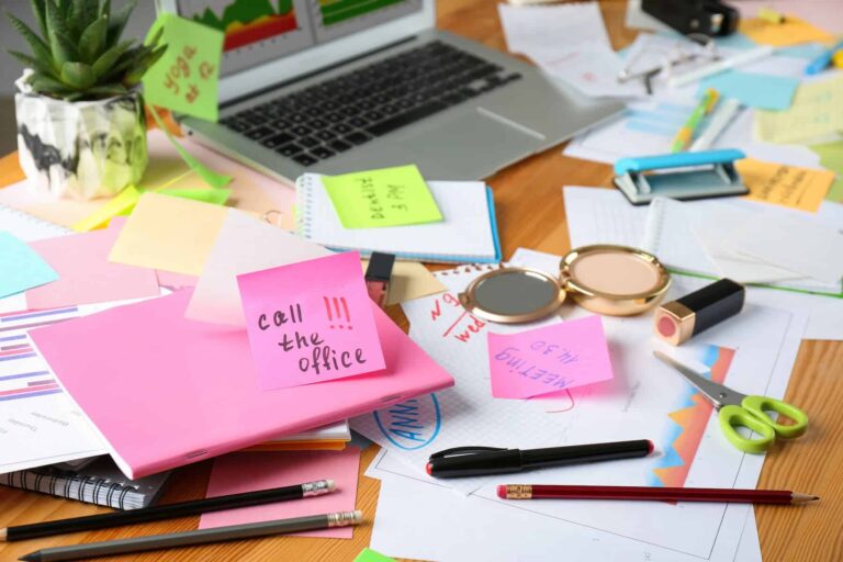 A messy table with a laptop, cosmetics, pens, and more, reflecting the concept of being overwhelmed by work and how clutter affects mental health.