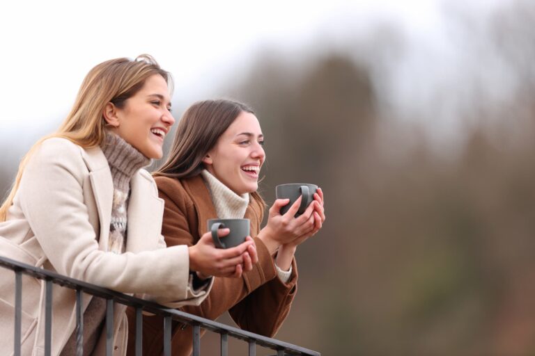 Two friends, one highly sensitive and the other an empath, relax on a balcony on a cold winter day, enjoying tea together.