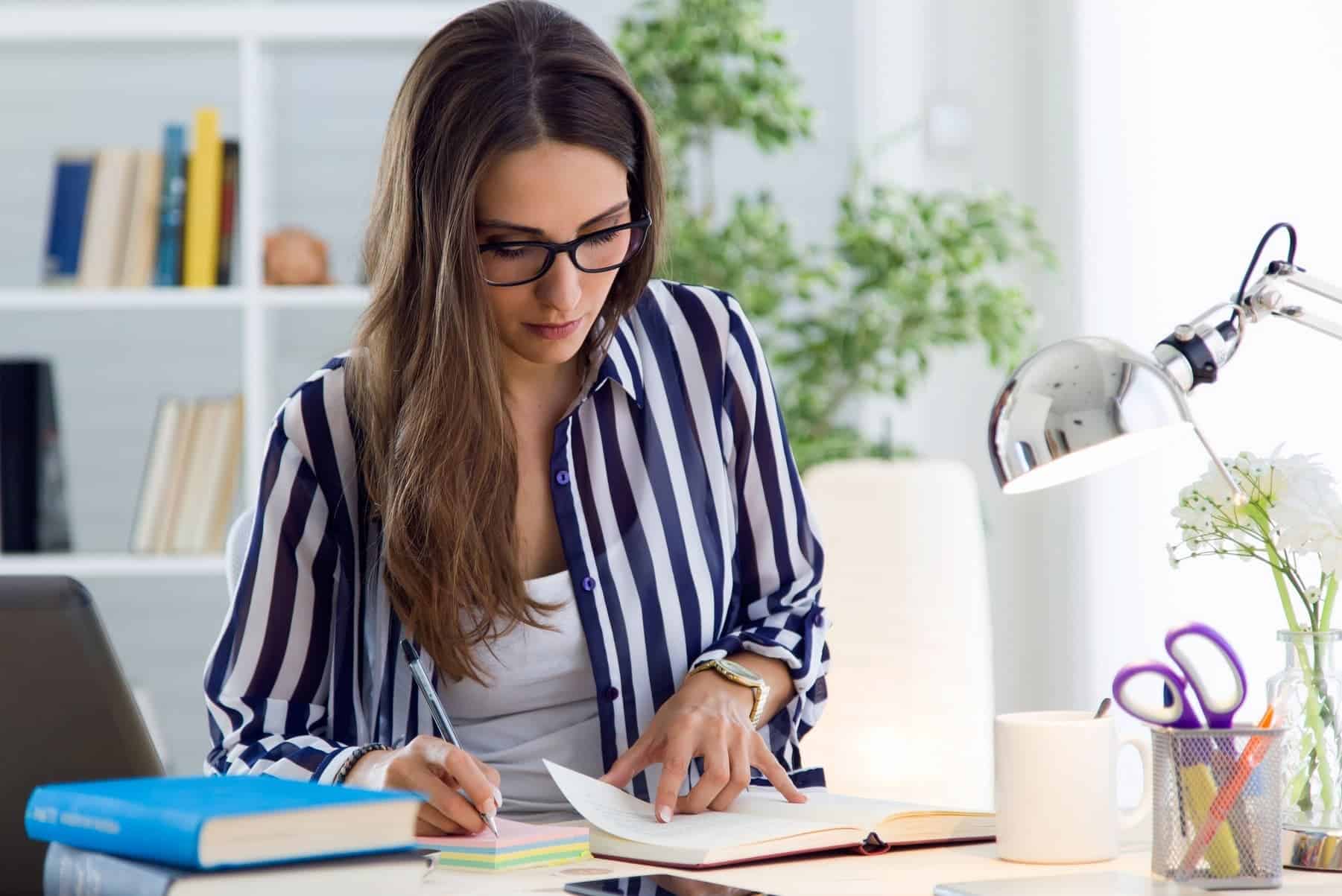 A woman in a blue and white striped blouse sits at her desk, working with strong focus, fully aware of the value of productivity and getting things done.