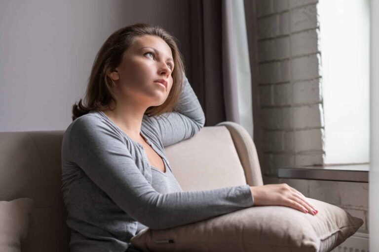 Woman sitting alone on a couch in deep thought, representing the emotional struggle with identity and self worth.