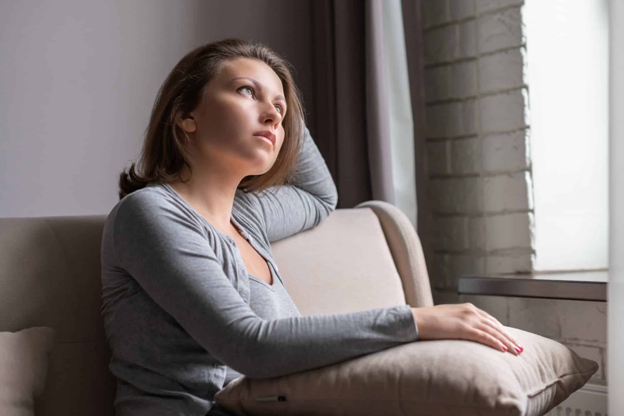Woman sitting alone on a couch in deep thought, representing the emotional struggle with identity and self worth.