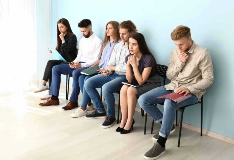 Several people sit in a waiting room with their CVs for an interview, some feeling like frauds, illustrating different types of imposter syndrome.