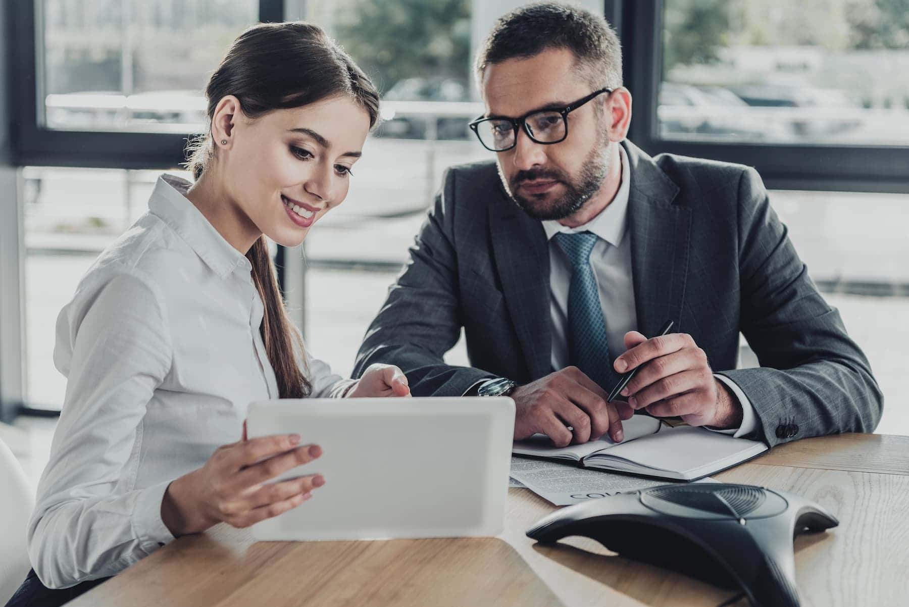 Two colleagues at a conference table reviewing a tablet, illustrating fixed mindset vs growth mindset with one looking optimistic and engaged while the other appears hesitant.