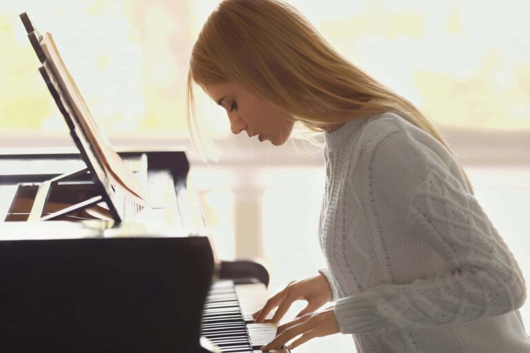 A woman practices piano in a cozy sweater, showing how to develop a growth mindset through learning and consistent skill-building.