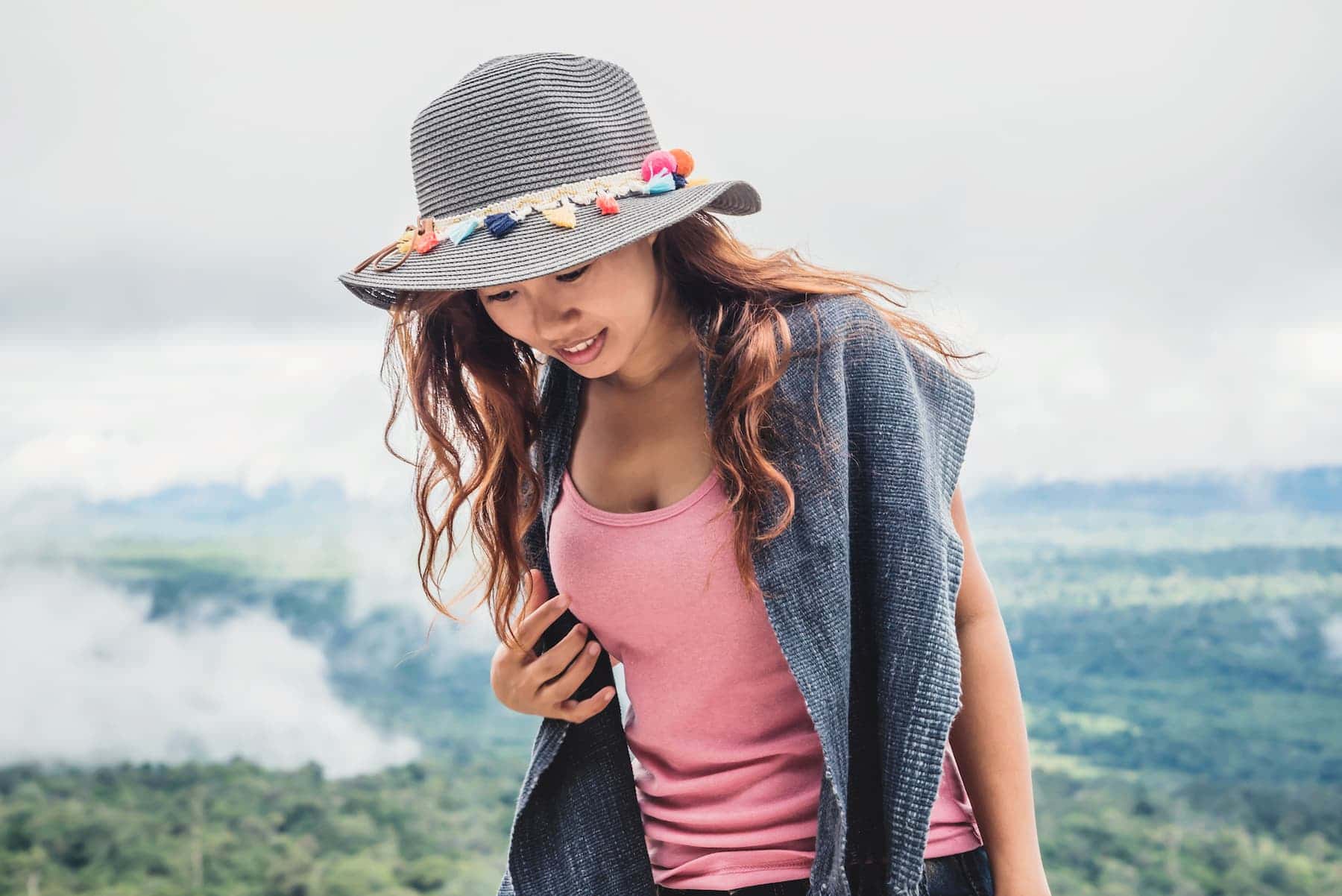 A woman in a striped hat and pink tank top smiles to herself, capturing the quiet, relatable moments of introvert humor.