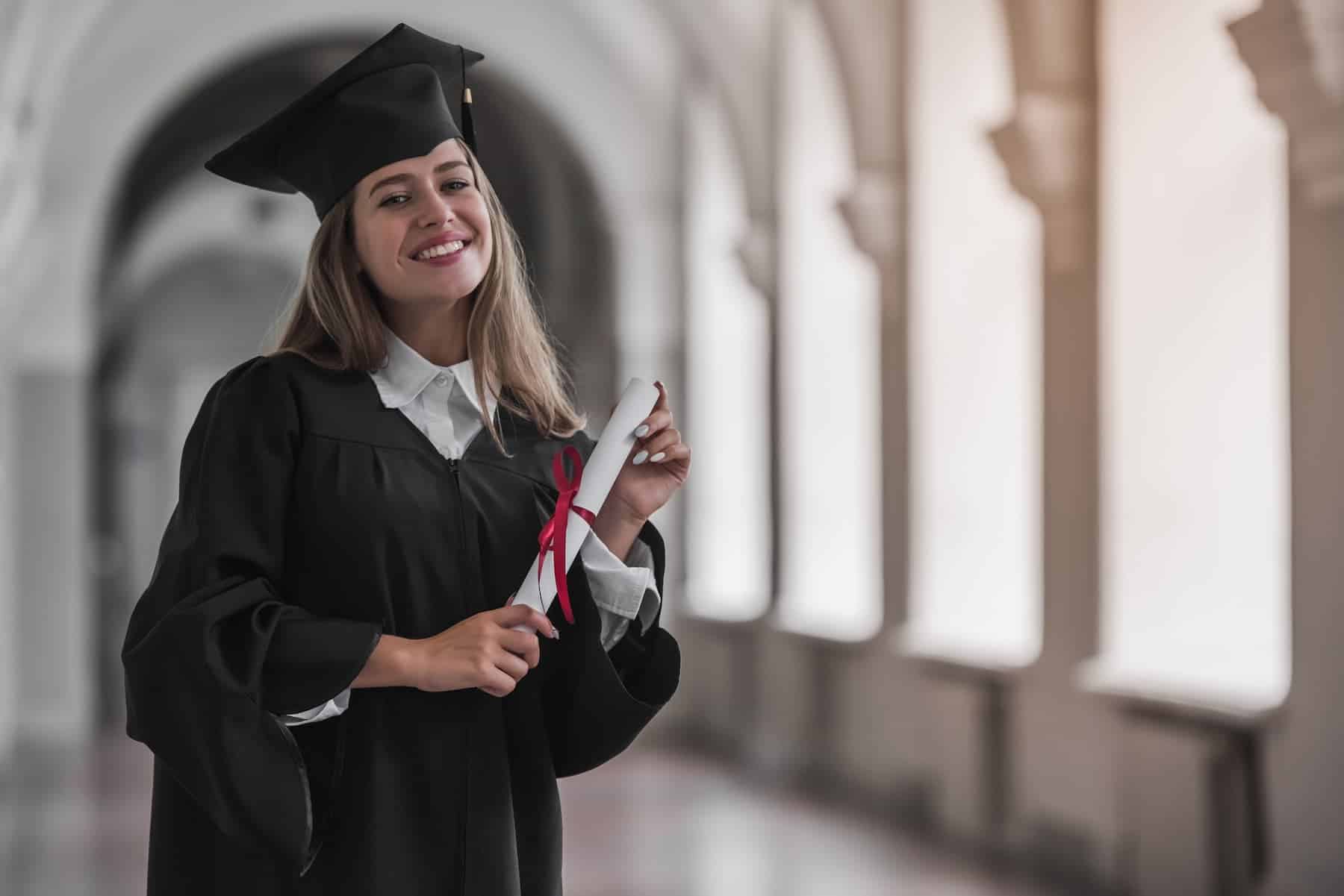 Graduate standing with diploma and cap in bright hallway, showcasing accomplishment and growth mindset background.
