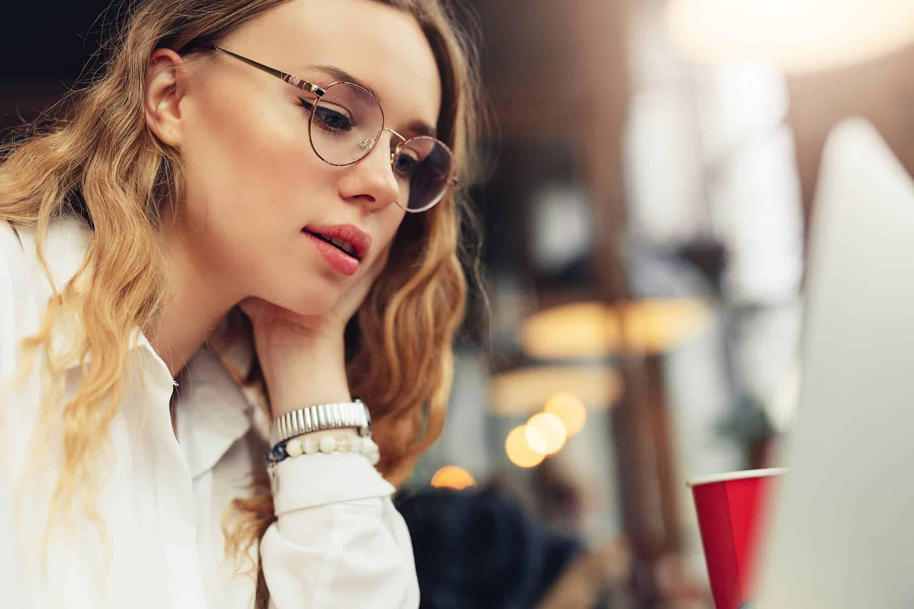 A woman sitting at a cafe thinking while looking at her laptop.