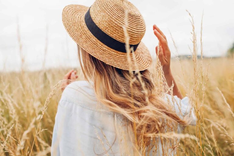 A woman with a straw hat is out in the field on a sunny day.