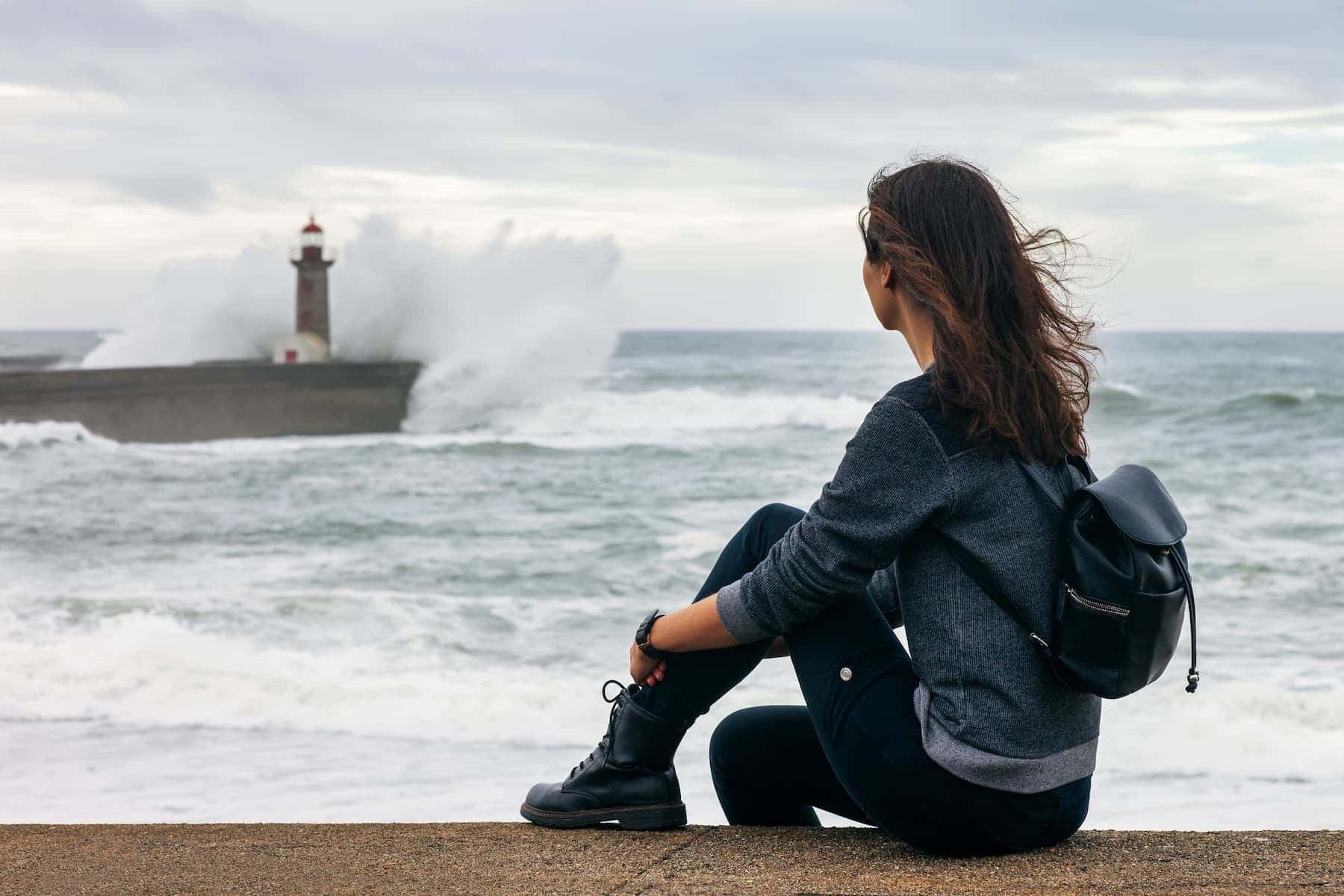 Solitary woman overlooking stormy sea and lighthouse, representing reflection and highly sensitive person traits.