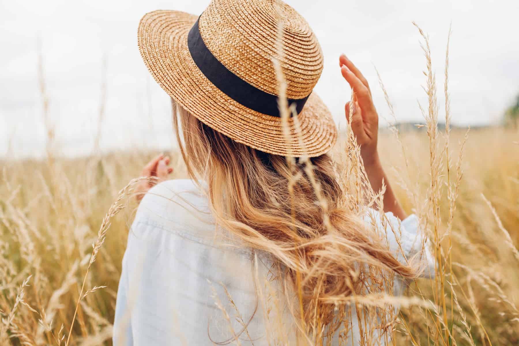 A woman with a straw hat is out in the field on a sunny day.