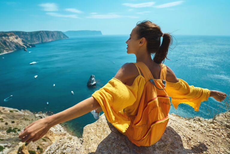 Woman with backpack on cliff edge above blue ocean, symbolizing exploration and quantum physics for beginners.