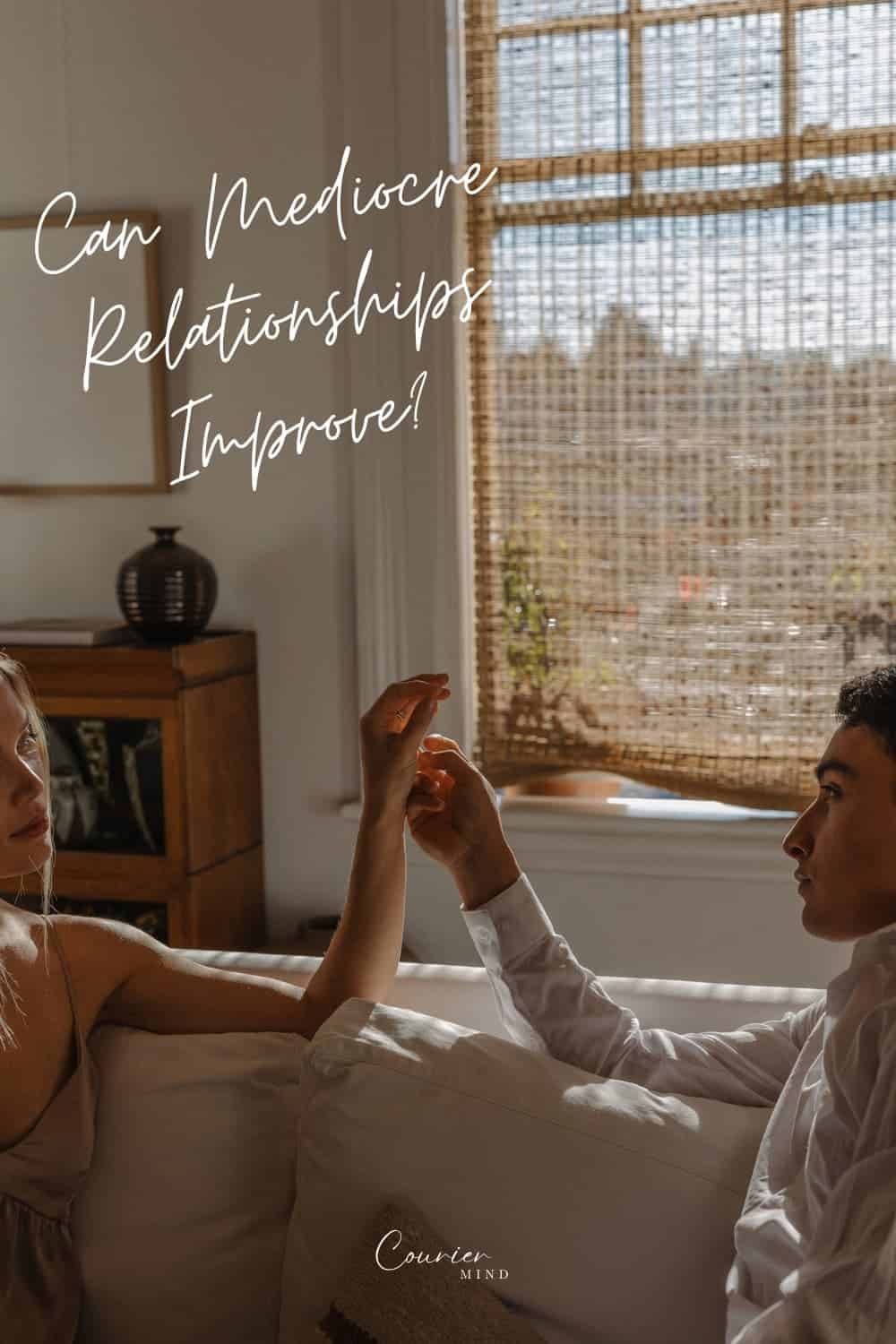 Couple holding hands on a couch, wondering whether a mediocre relationship can still be saved.