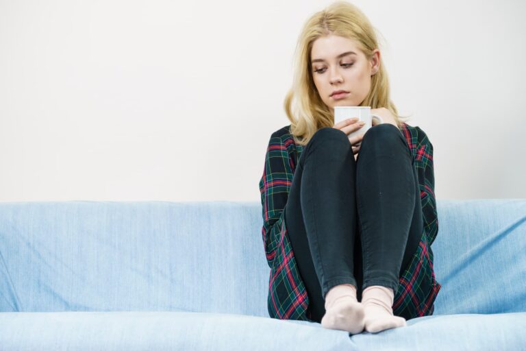 Woman sitting on the couch feeling sad because she couldn't leave her comfort zone.