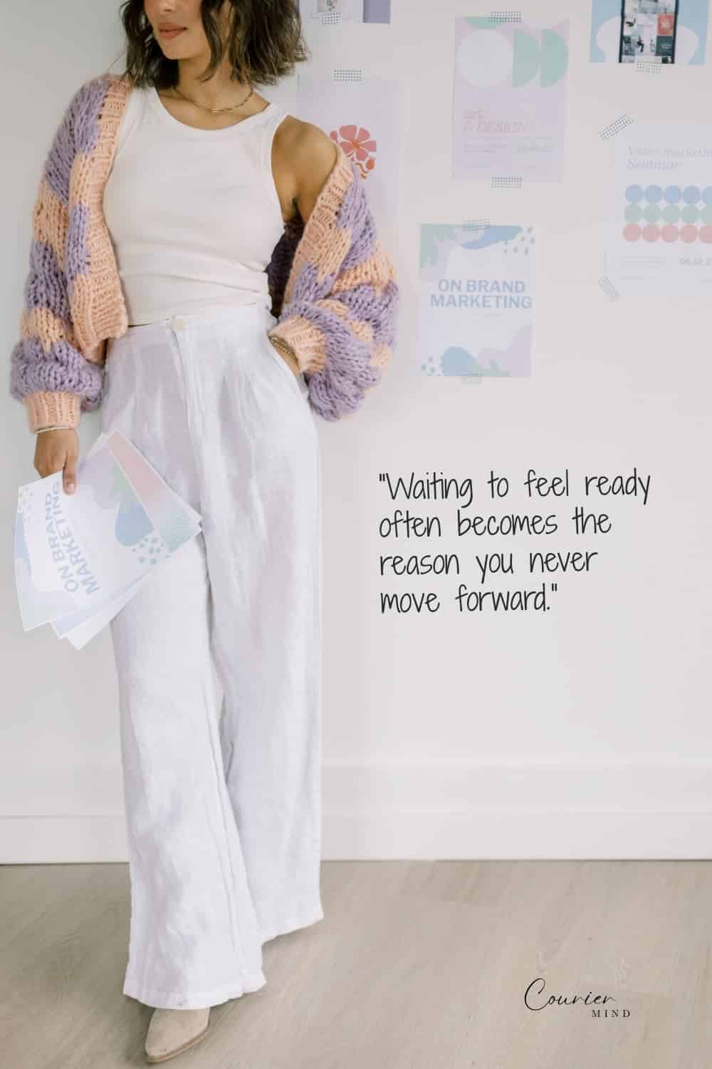 Woman in a white tank top, wide-leg pants, and knit cardigan holding papers while planning her next steps.