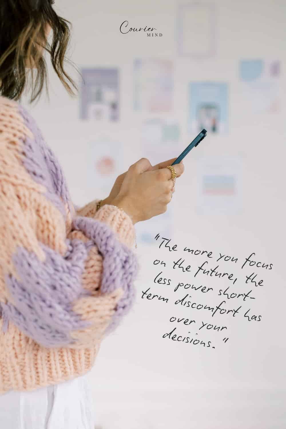 Woman in a striped knit sweater holding a smartphone while reviewing ideas and opportunities for personal growth.
