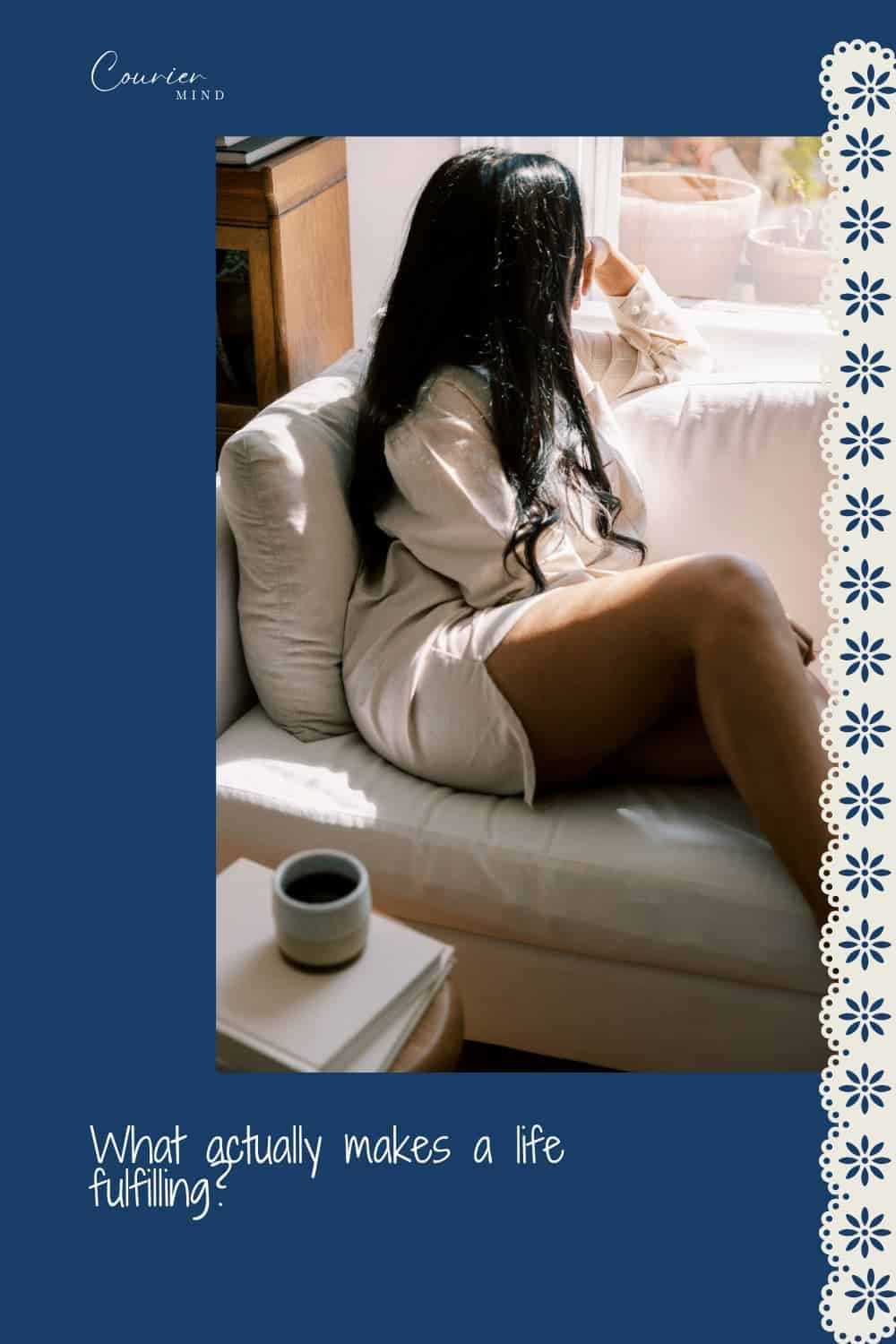 Woman with long dark hair sitting on a white sofa and looking out a window.